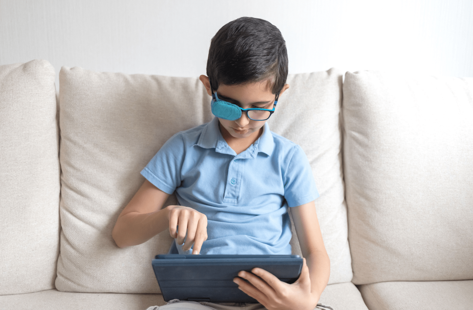 A boy wearing eyeglasses with a patch on the right lens while using his iPad