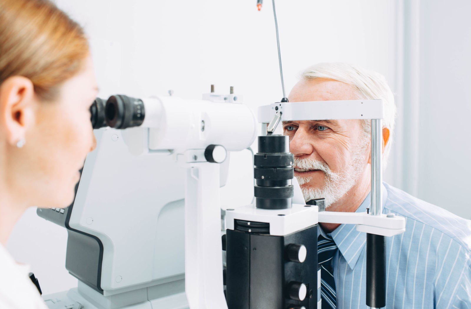 A female optometrist using equipment to look inside a male patient's eyes