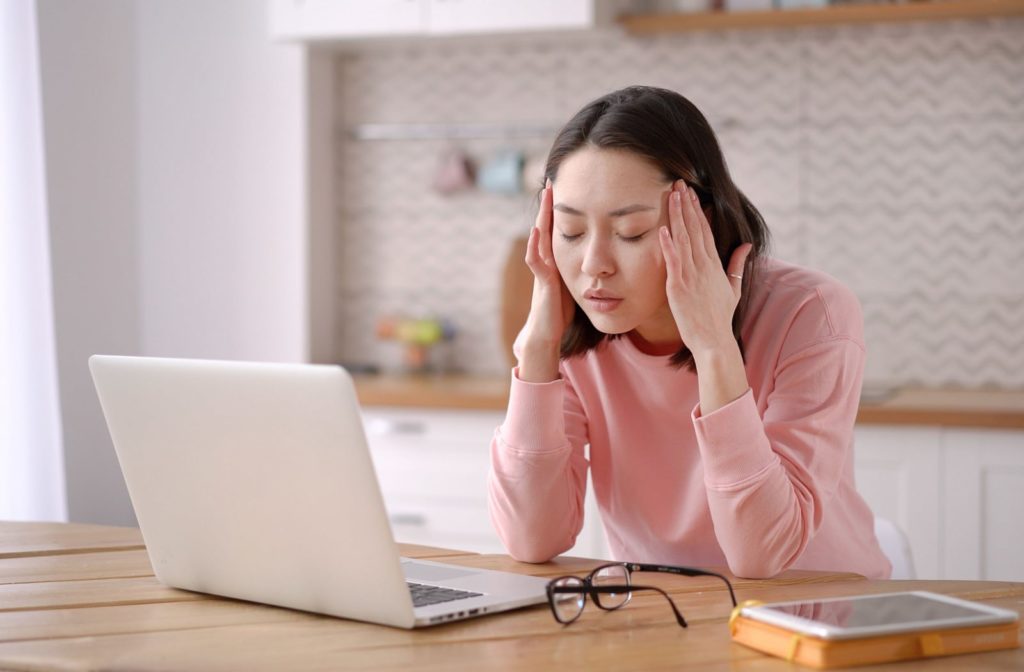 A young woman is massaging her temple with her eyes closed. Taking a break from the computer screen to relax her eyes