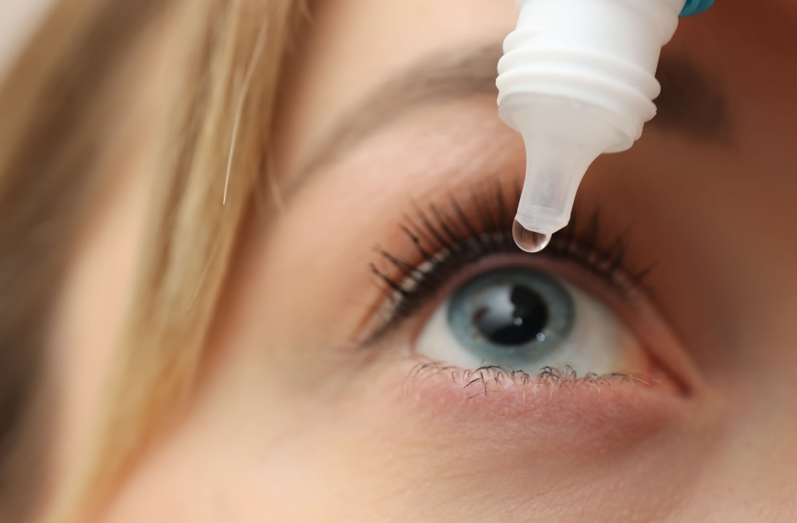 A close-up of a young woman using eye drops.