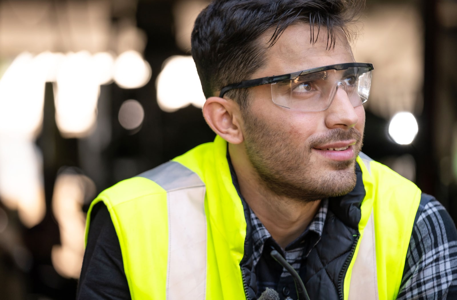 A man wearing a yellow safety vest and safety glasses at his job.