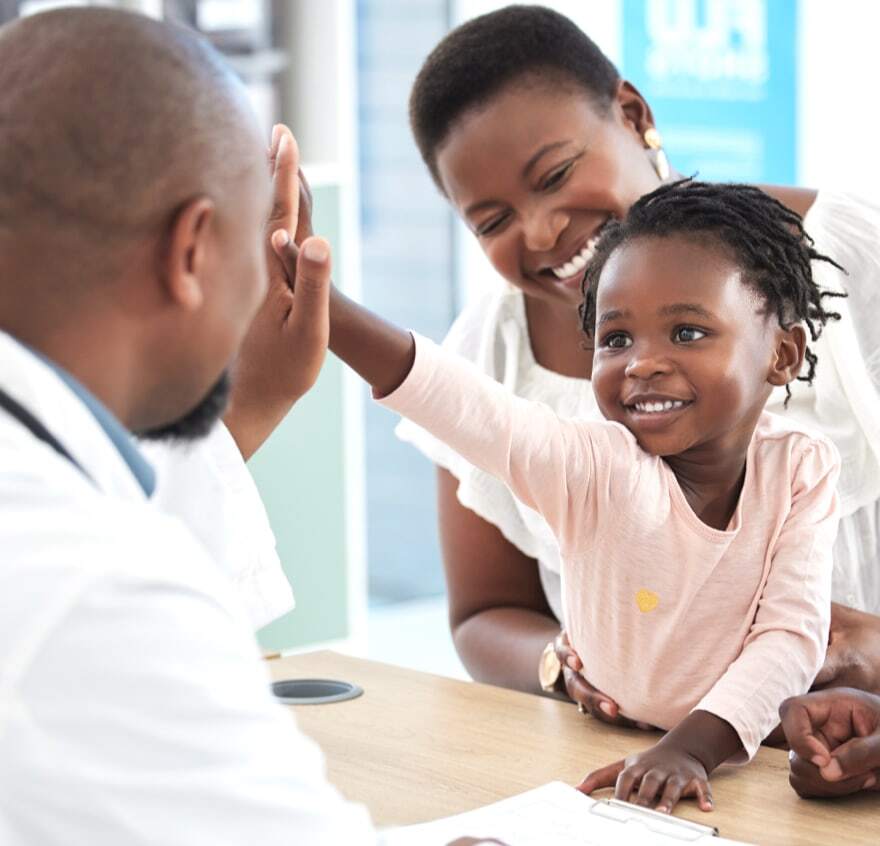 A mother sits with her daughter while an optometrist gives the girl a high five