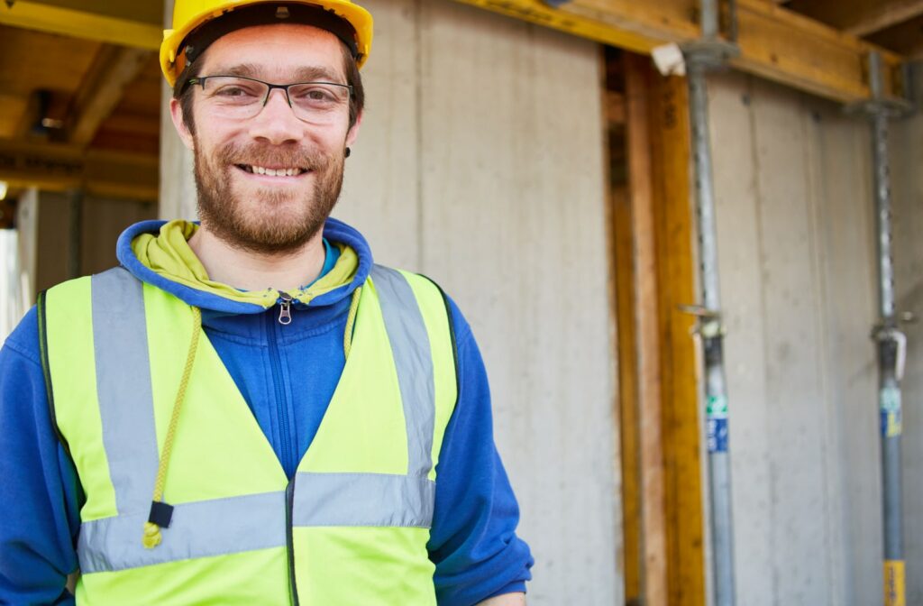 A construction worker on a construction site, smiling at the camera while he is wearing prescription safety glasses