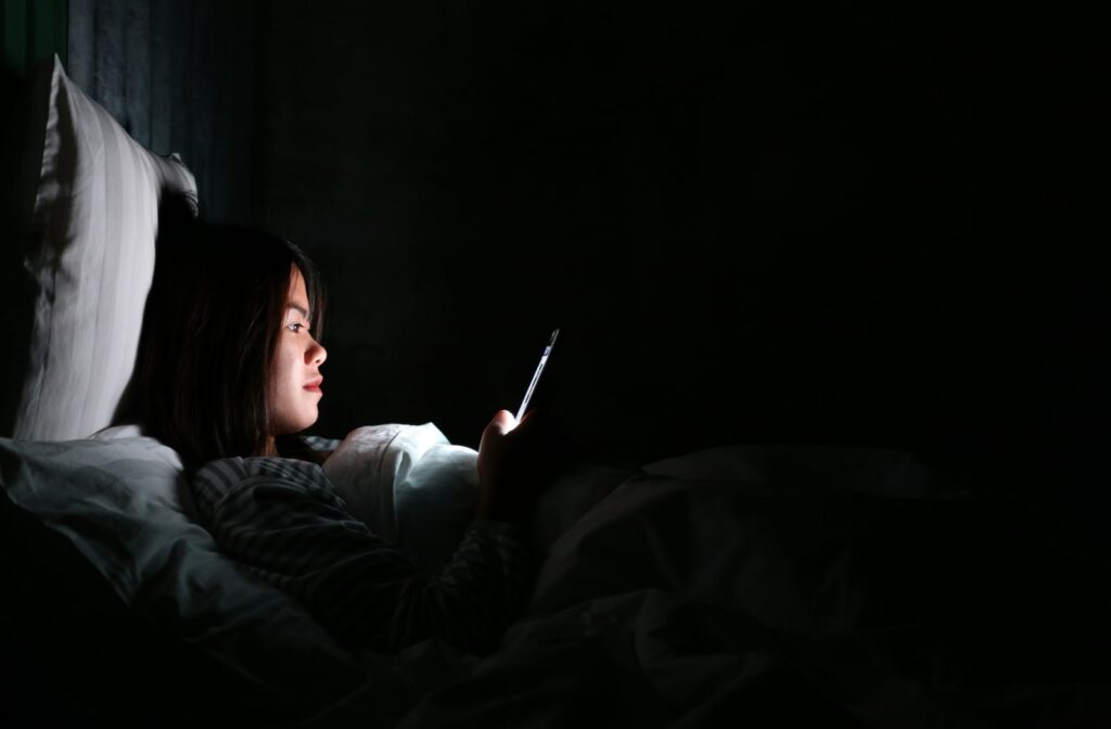 A woman laying in bed and using her phone in a very dark room.
