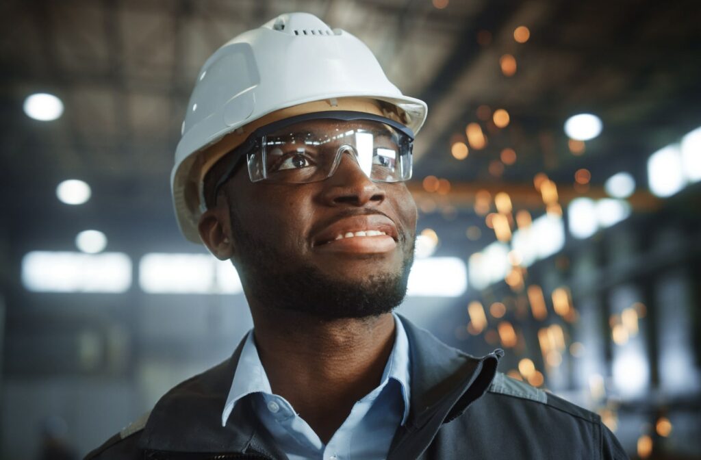 A young man smiling and looking upwards while wearing prescription safety glasses and a hard hat while working