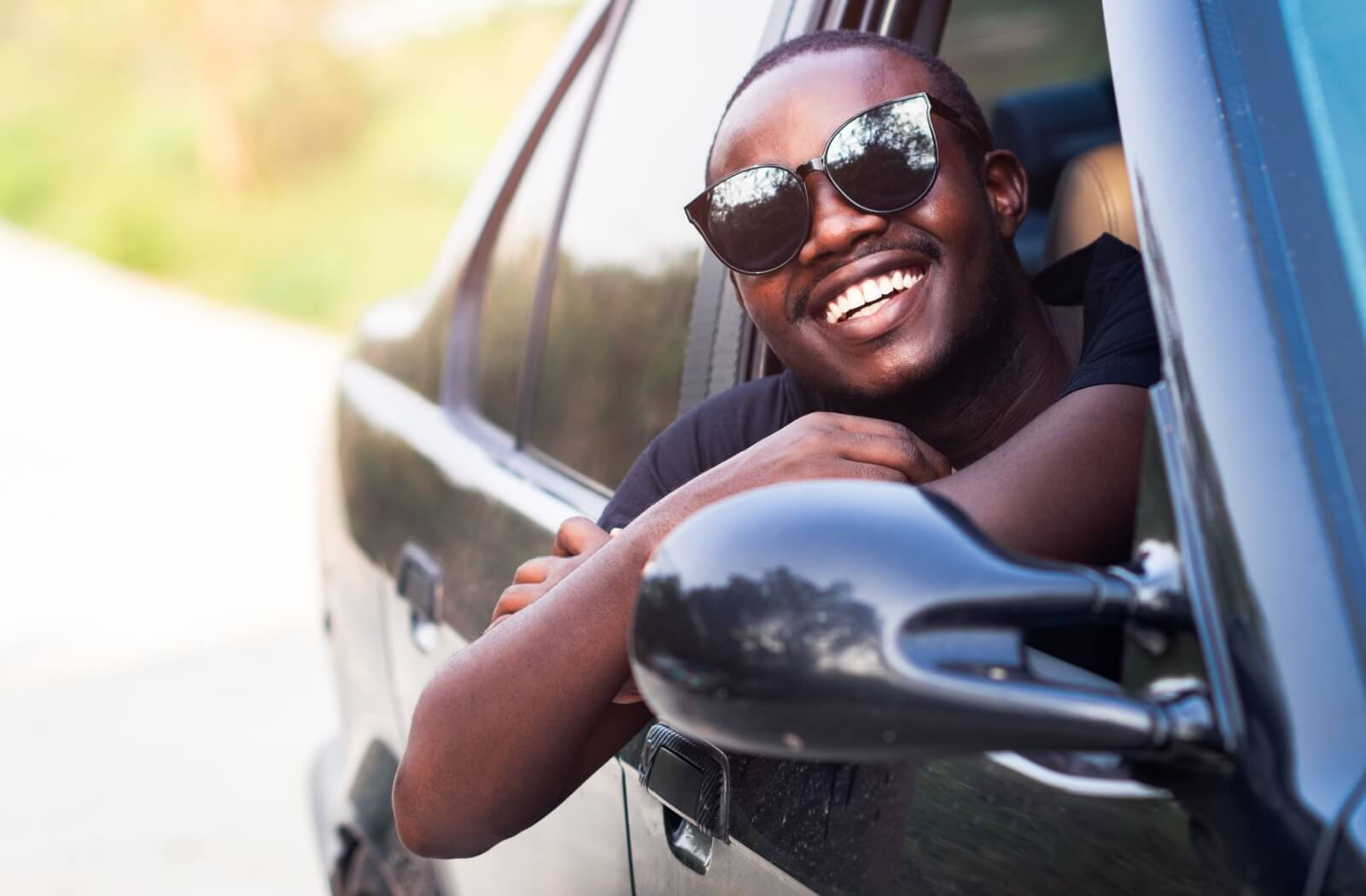 Young man wearing sunglasses smiling in a car.