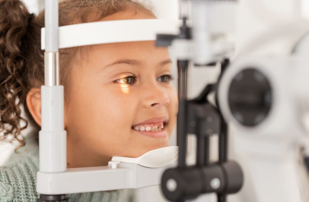 A little girl smiling during a slit-lamp exam at an eye exam to find the right myopia control option.