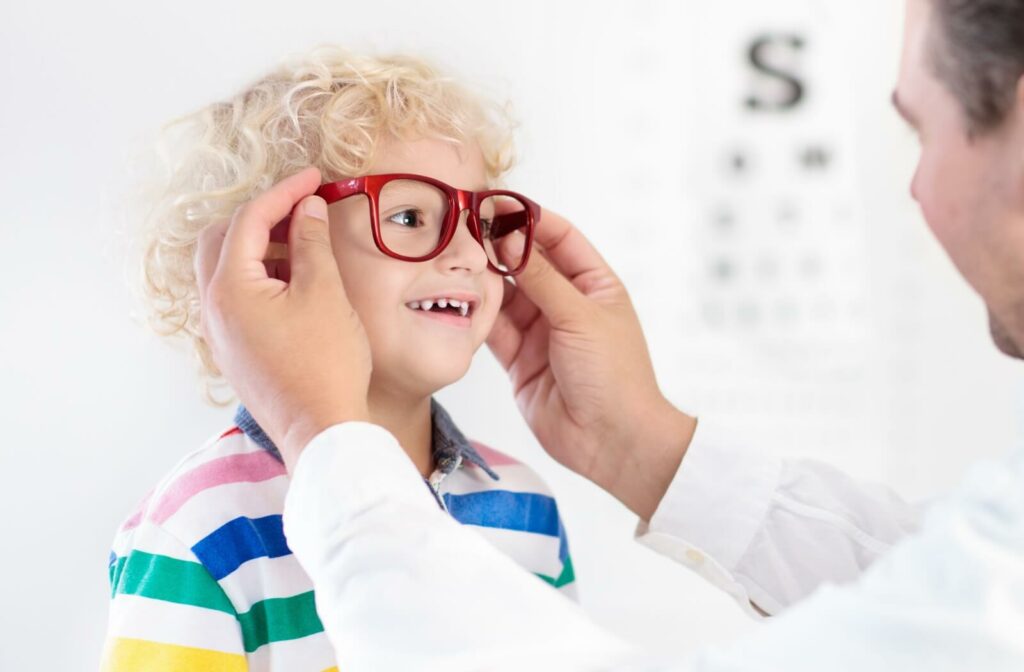 An eye doctor placing glasses on a smiling boy's face.