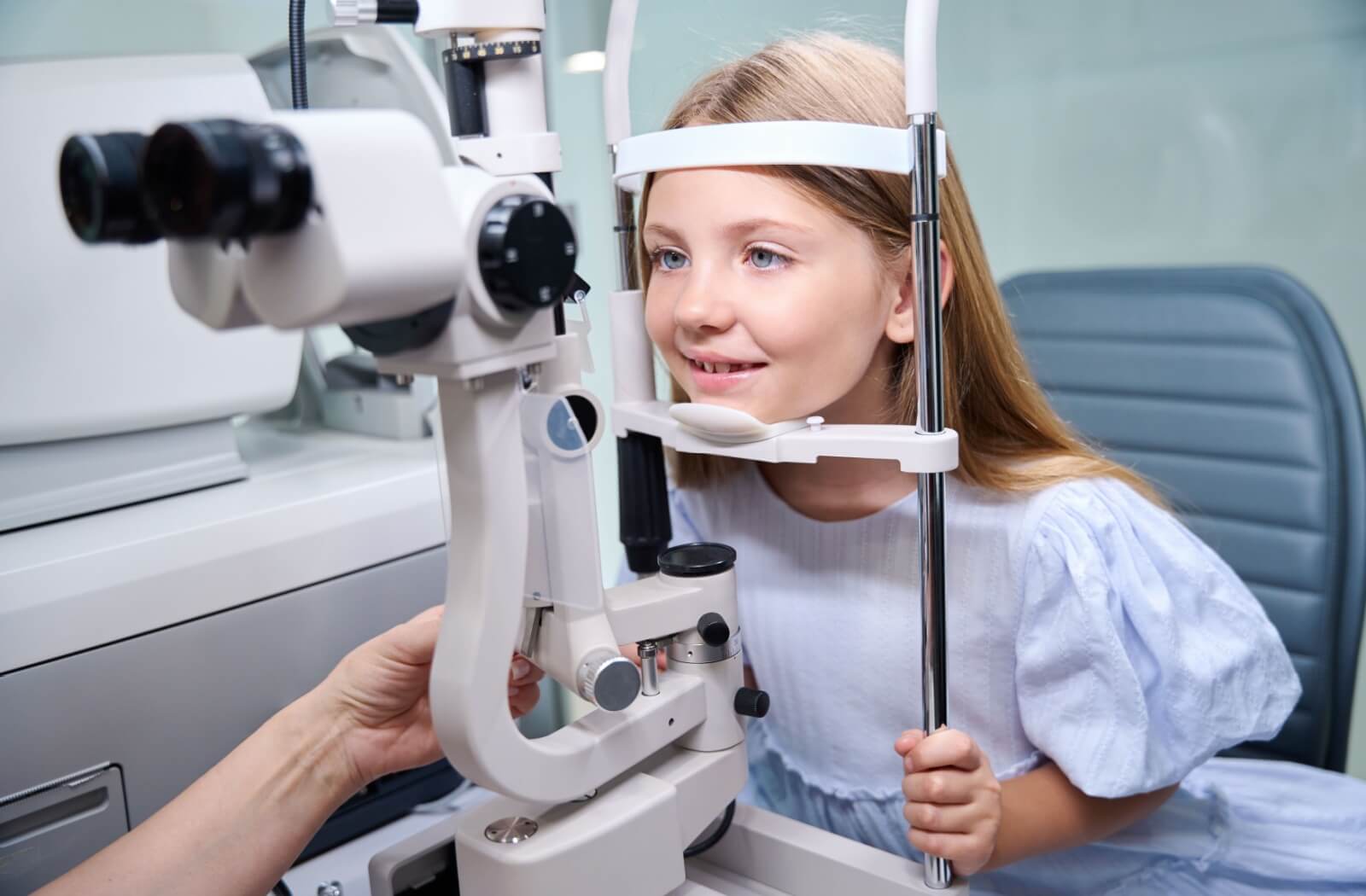 A little girl smiling while an out-of-frame optometrist examines her eyes during an eye exam.