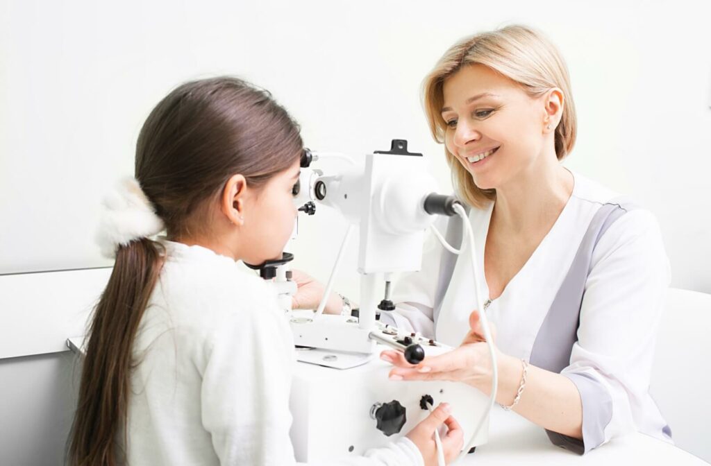 An optometrist smiling while showing a little girl strabismus testing equipment during an eye exam.
