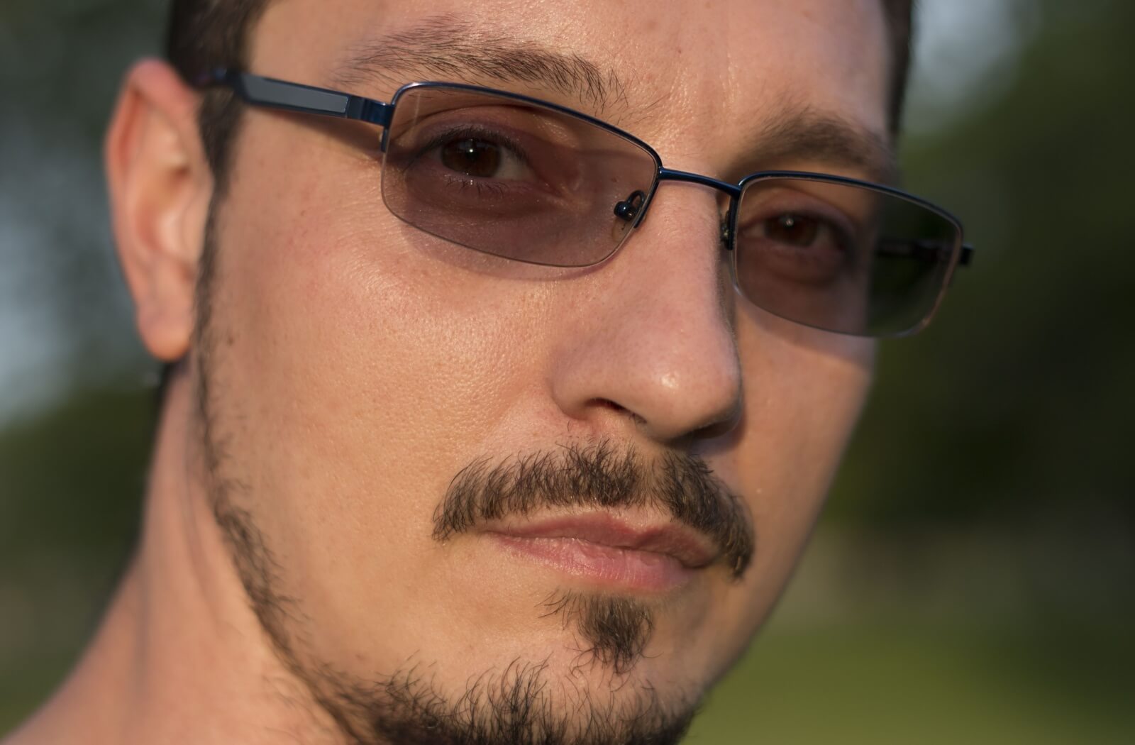 A close up man's face wearing transition lenses outdoors.