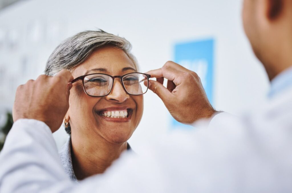 Optometrist placing glasses on a person smiling.