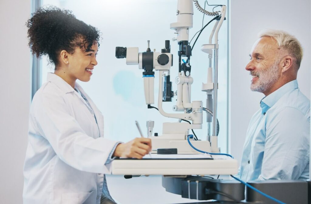 An optometrist smiles while examining their patient's eyes carefully during an eye exam in a white office.