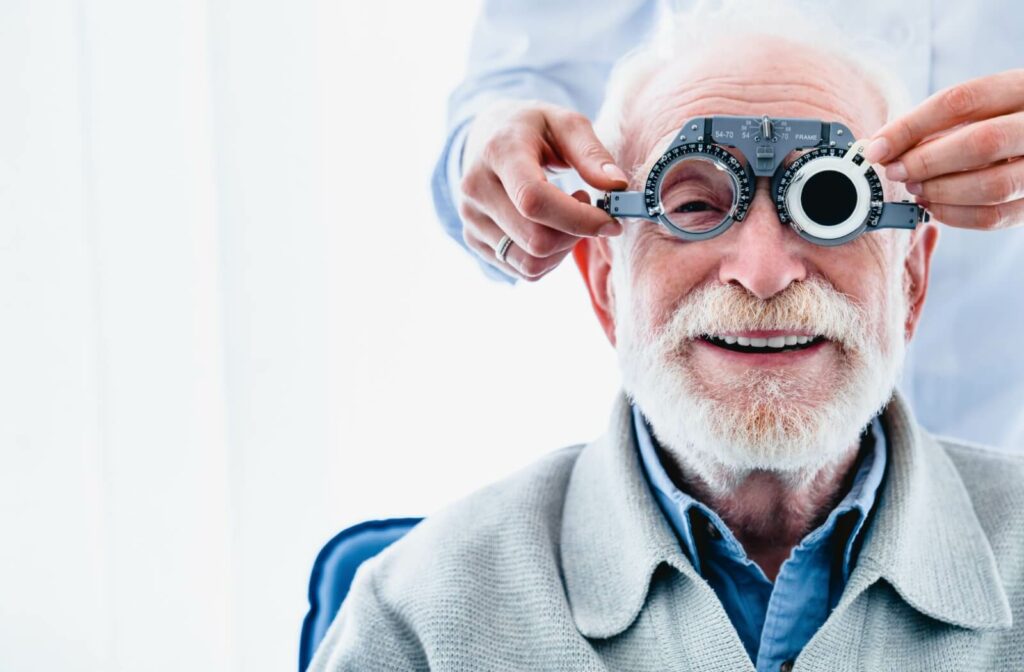 Smiling older patient undergoing an eye test with a phoropter, guided by an optometrist.