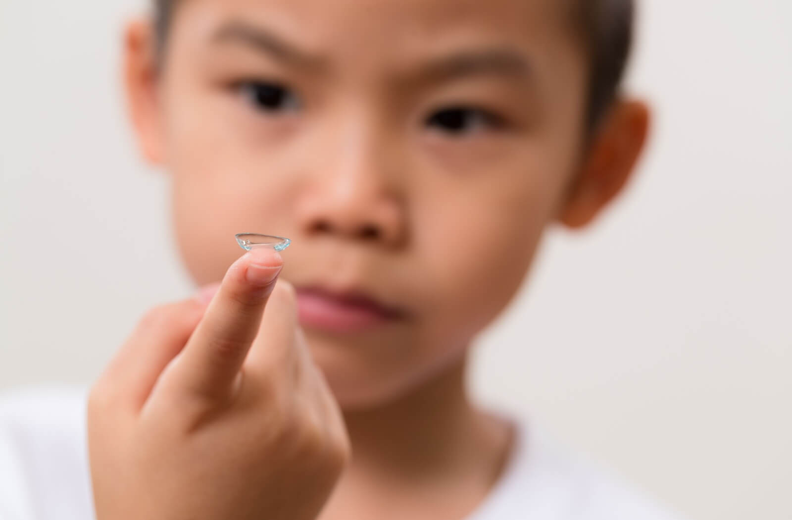 A young child with myopia holding up a contact lens on their finger against a white background.