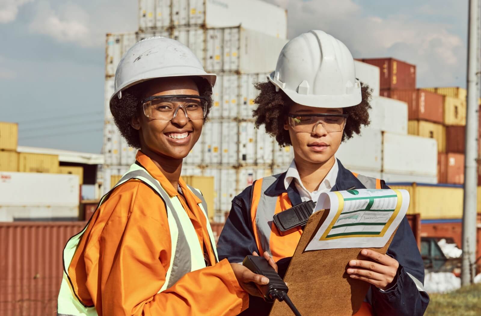 Two women wearing Onguard safety glasses stand outdoors at a construction site.