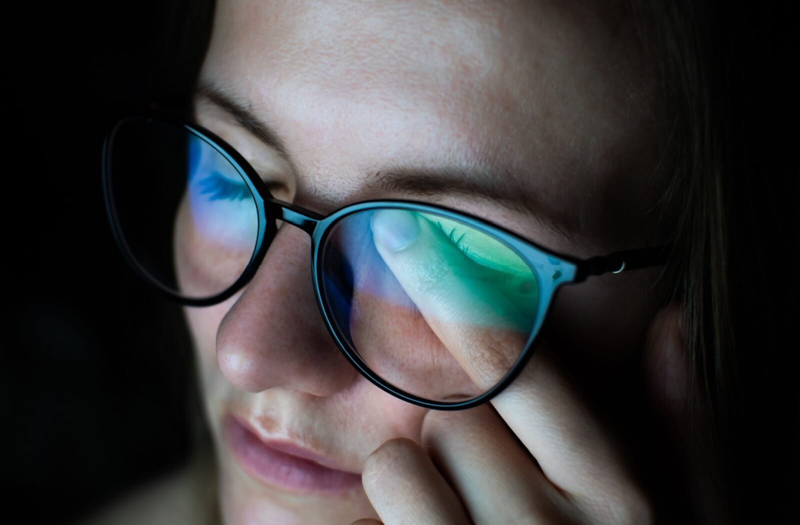 Woman rubbing her eye while wearing glasses, showing signs of eye discomfort possibly related to dry eye or blurry vision.
