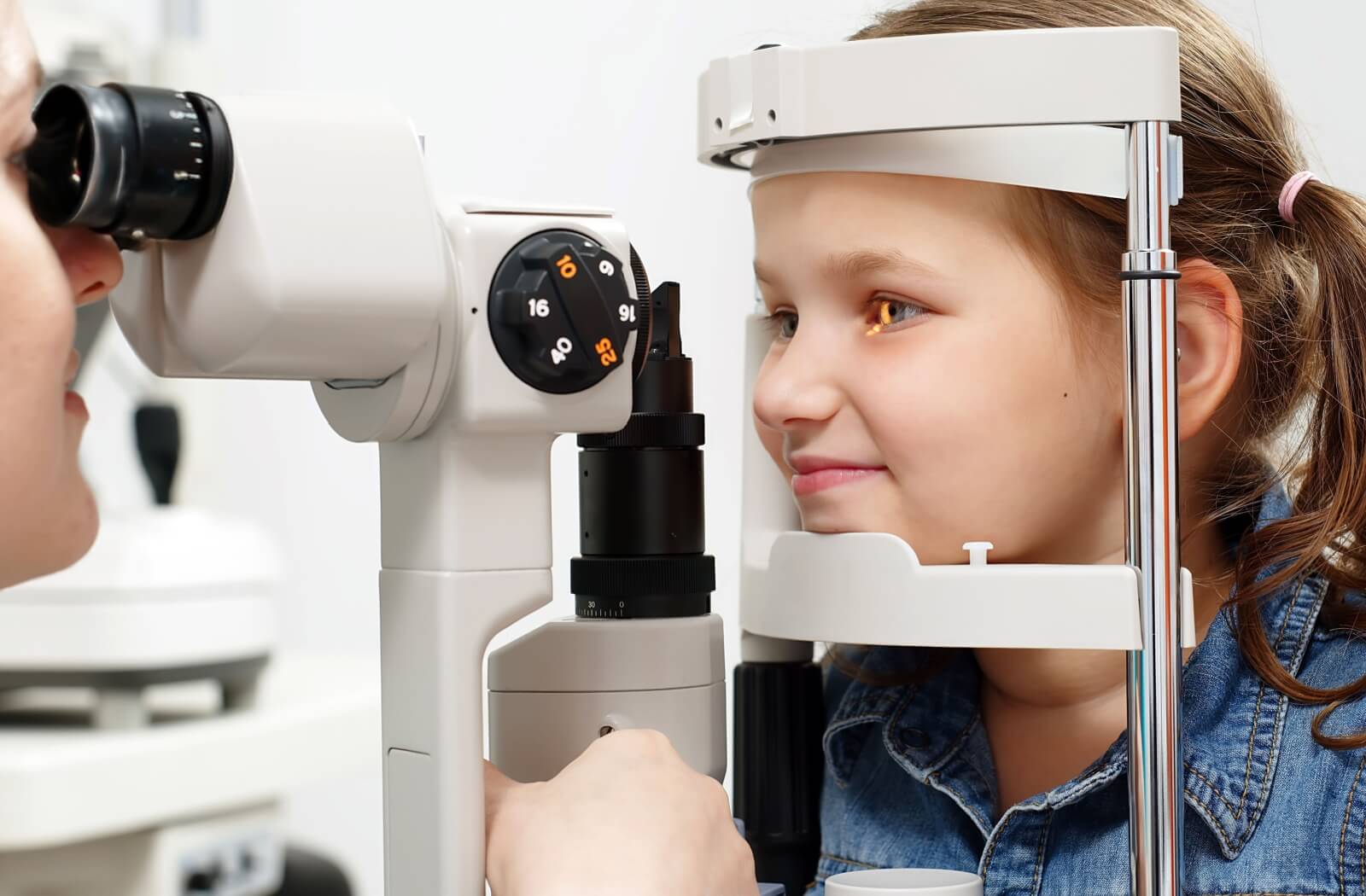 A young child smiles during a routine eye exam as their eye health is checked using a slit lamp.