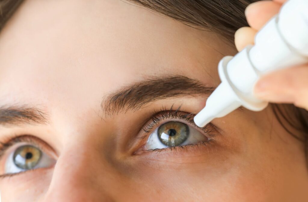 A person applying eye drops to their eye for relief from dry eyes, holding the dropper near the eyelid and carefully administering the drops. The focus is on the person’s eye and the bottle.